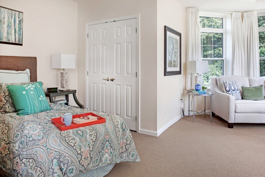 A cozy bedroom with a colorful bedspread, a tray on the bed, and a large window providing natural light.