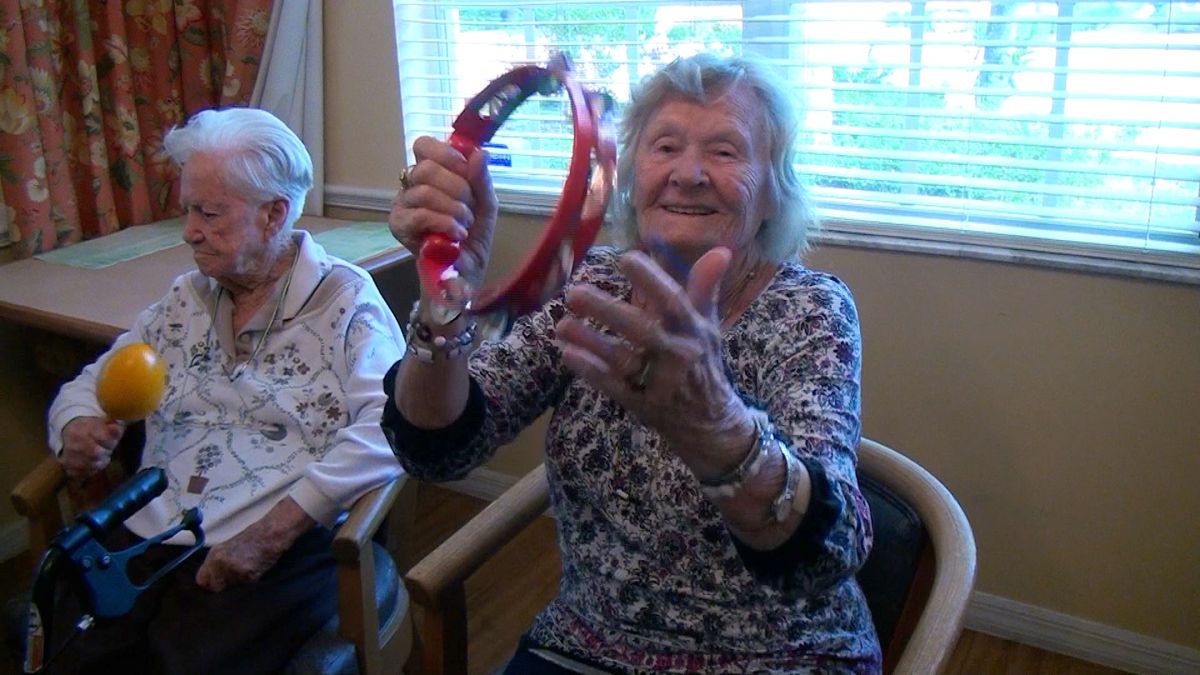 An elderly woman joyfully playing a tambourine during a group activity.