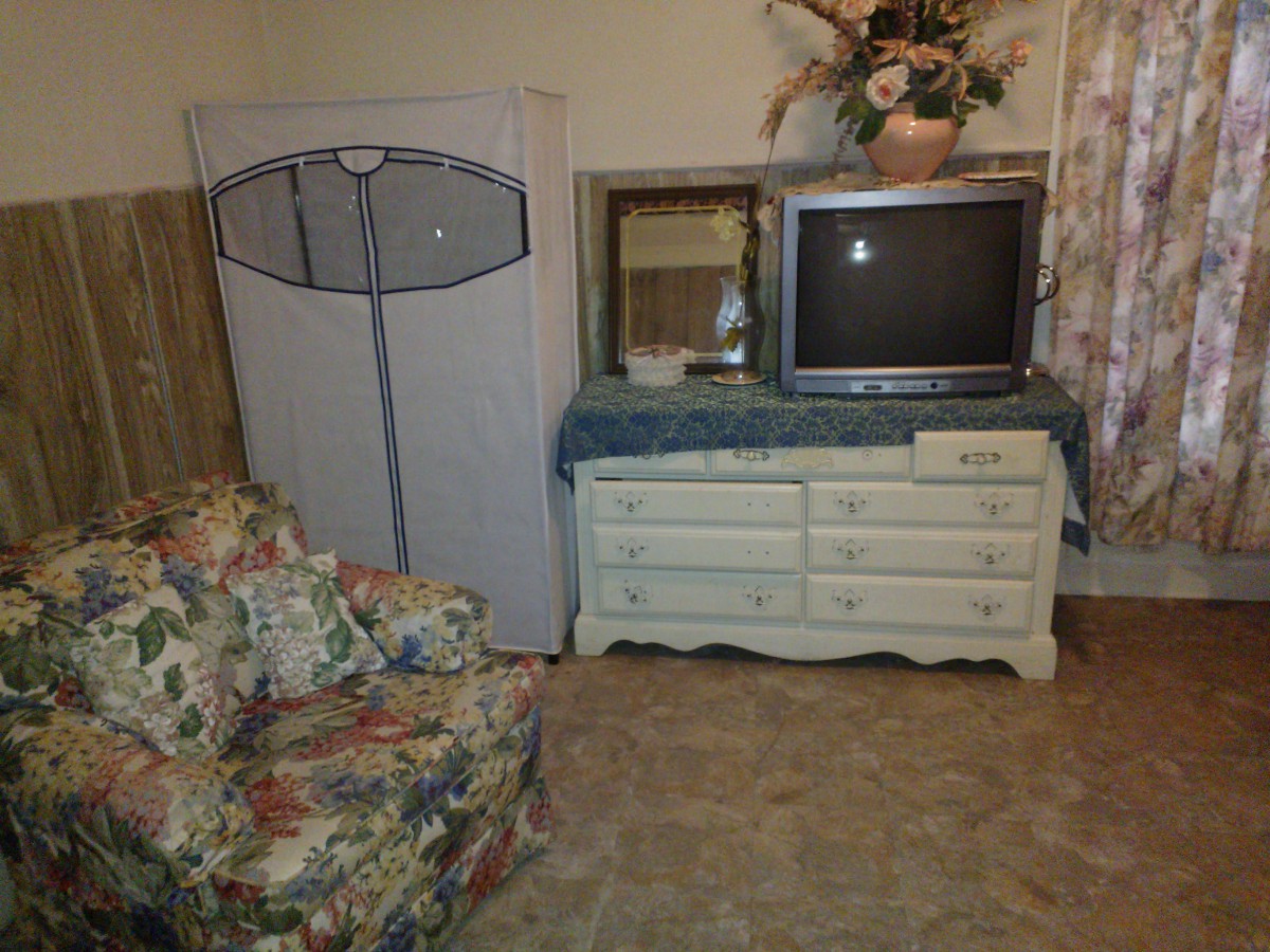 A cozy living room corner with a vintage TV on a dresser, a floral armchair, and decorative elements.