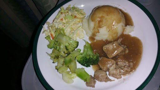 A delicious plate of comfort food featuring mashed potatoes with gravy, chicken, steamed broccoli, and a refreshing cabbage salad.