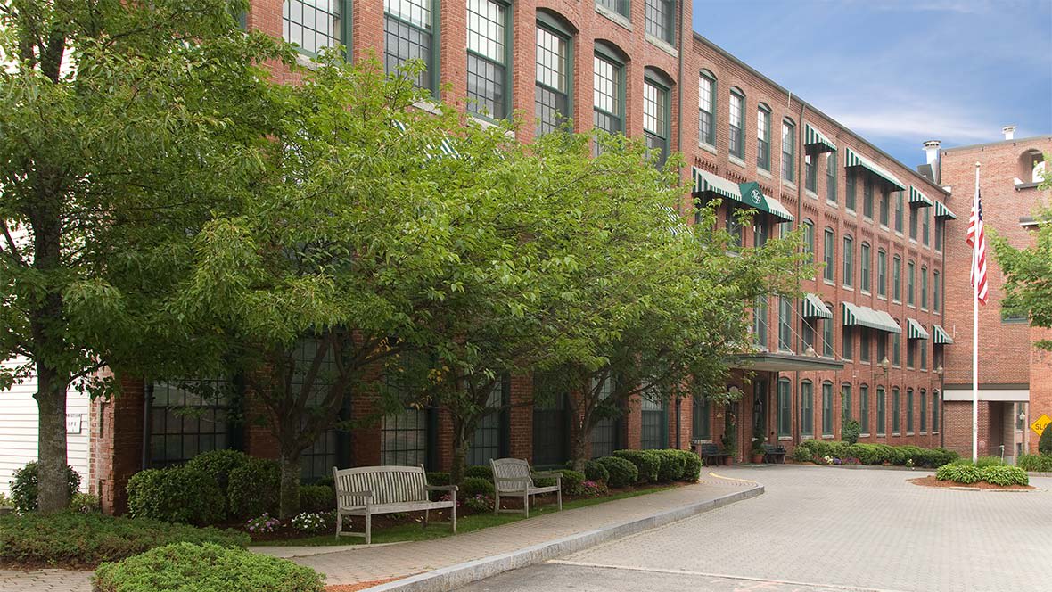 A brick building lined with trees and benches along a quiet sidewalk.
