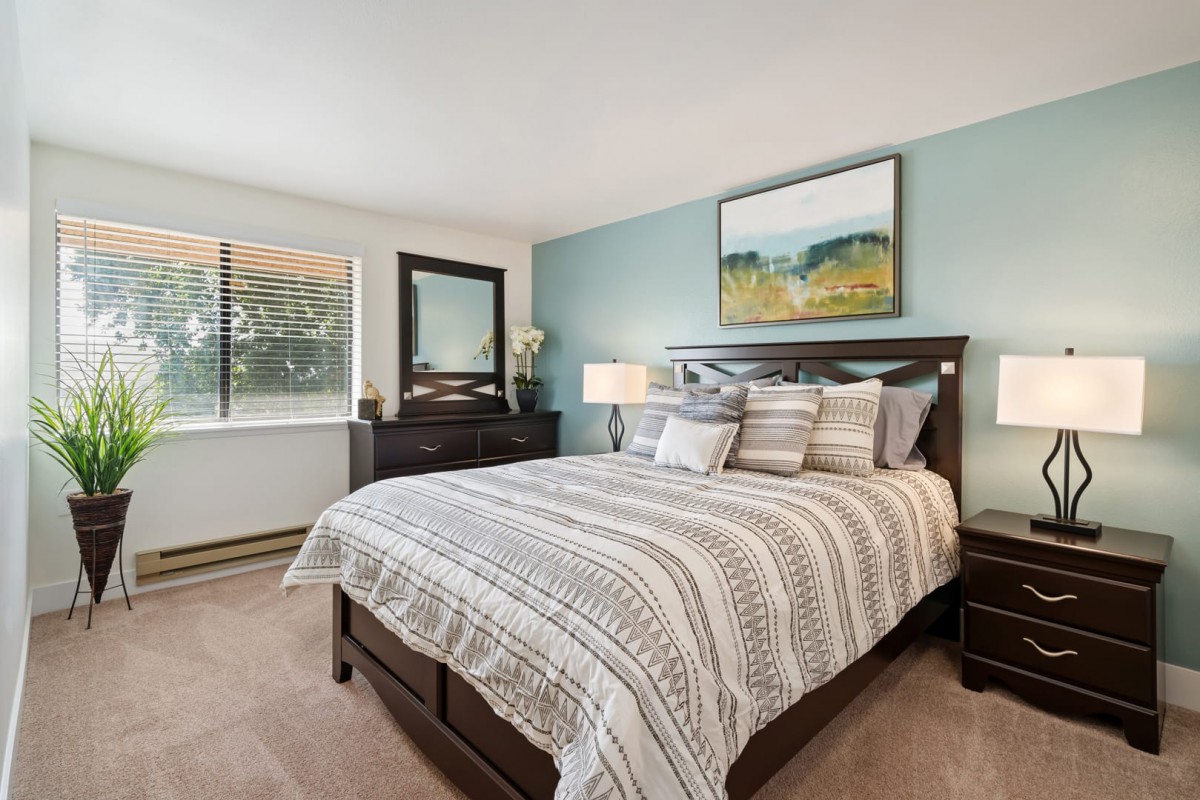 A cozy bedroom with a neatly made bed, a dresser, and a painting above the headboard.