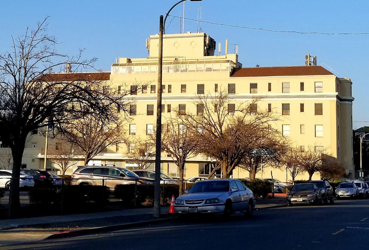 A large hospital building with parked cars and trees on a sunny day.