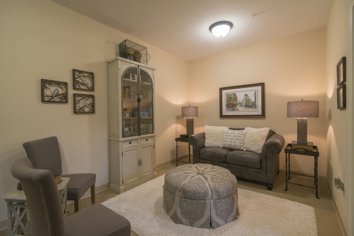 A cozy living room with vintage-style decor, featuring a sofa, cabinet, and an upholstered ottoman.