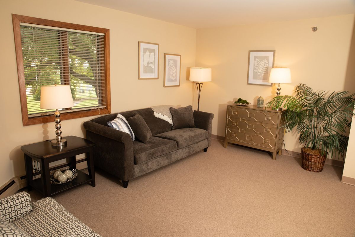 A cozy living room with a brown sofa, two floor lamps, and framed artwork on the walls.