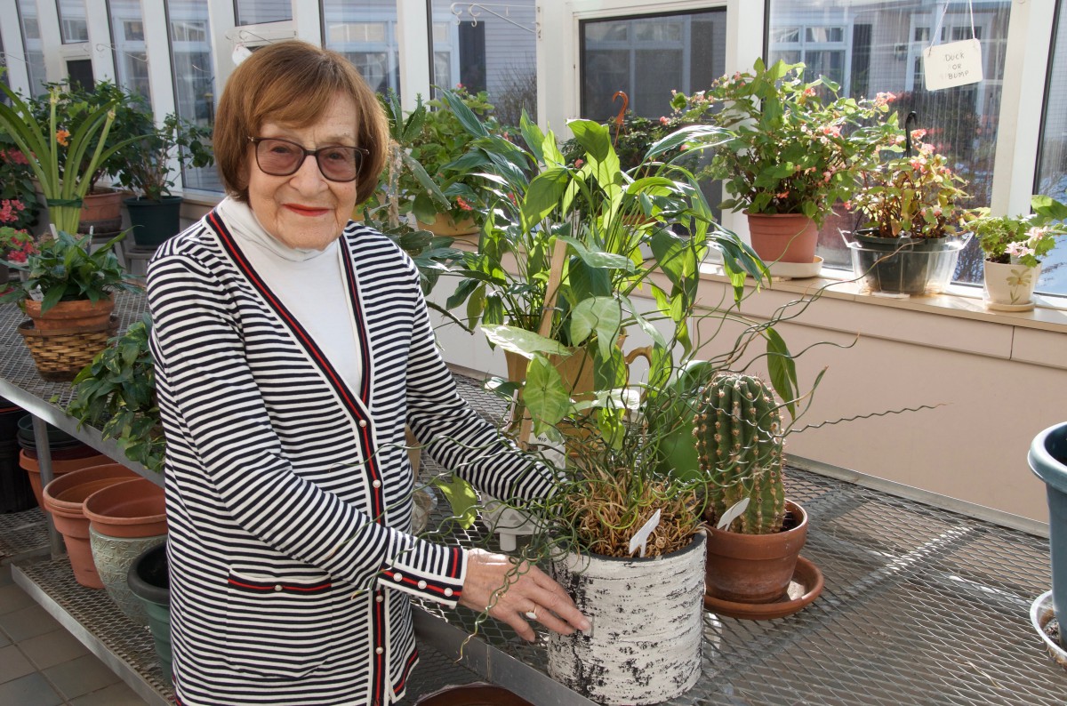 A woman standing in a greenhouse, holding potted plants including a cactus.