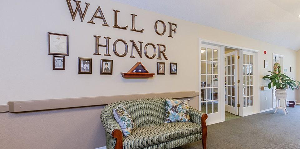 A cozy interior space featuring a 'Wall of Honor' with framed photos and a folded flag, complemented by a patterned couch.