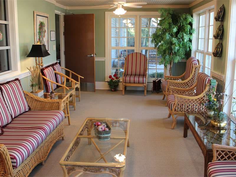 A cozy living room featuring rattan furniture, a glass coffee table, and large windows.