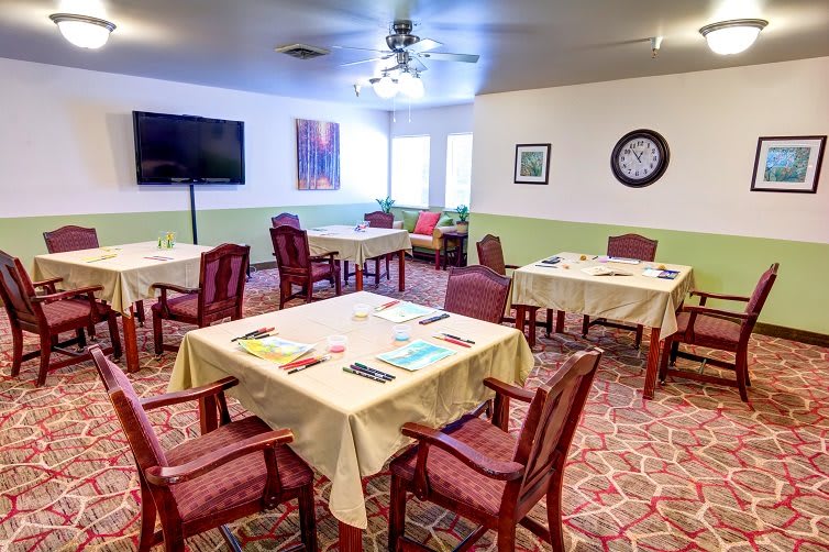 A well-organized dining room with multiple tables and chairs, featuring a television, artwork, and a wall clock.