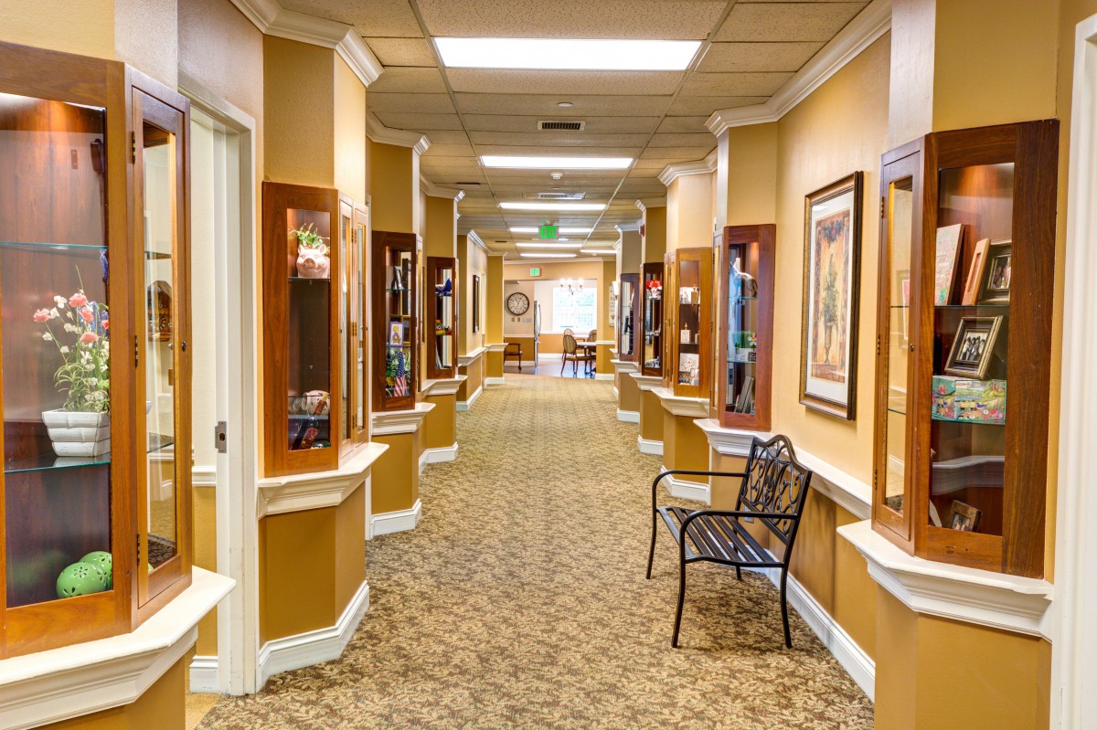 A well-decorated hallway with framed art and seating, leading to a bright area at the end.