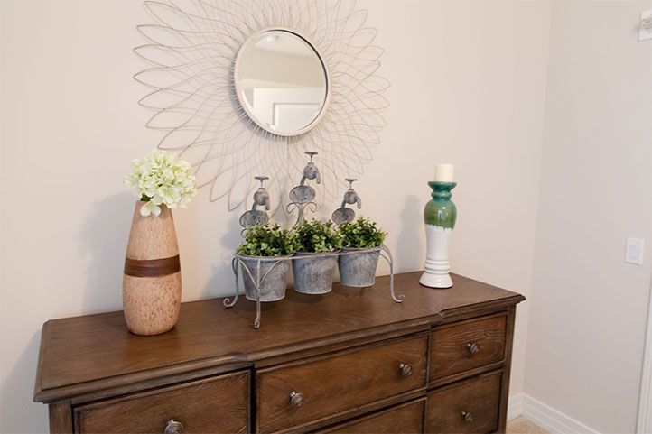 A decorated dresser featuring a mirror, plants, a vase, and a candlestick.
