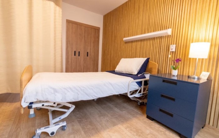 A modern hospital room with a neatly made bed and stylish wood paneling.