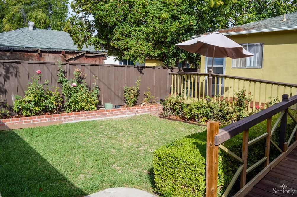 A cozy backyard with a grassy lawn, wooden deck, and shaded umbrella.