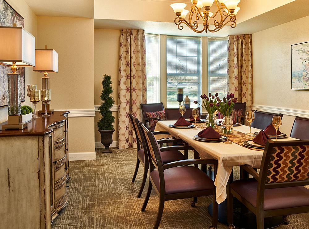 A warmly decorated dining room with a set table, chandelier, and elegant furnishings.