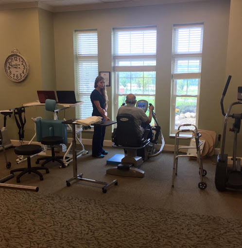 A physical therapy session in progress with a therapist assisting a patient by the window.