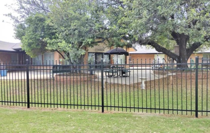 A suburban house with a fenced patio area, outdoor furniture, and surrounding trees.