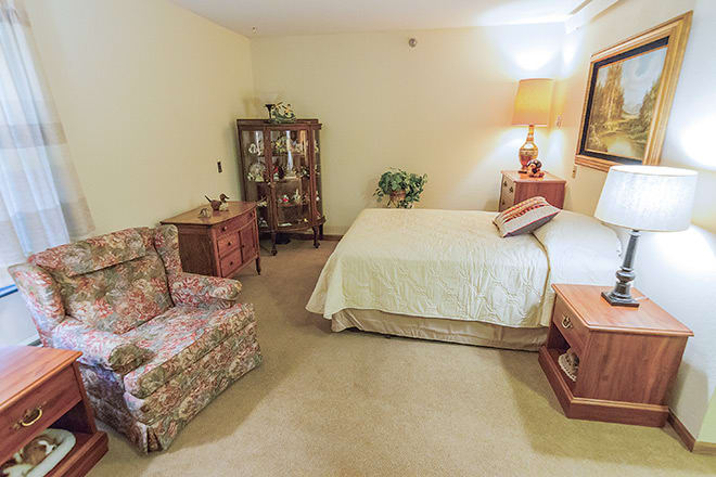A cozy bedroom featuring vintage decor with a bed, armchair, and cabinet.