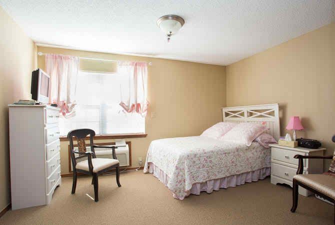 A cozy bedroom with a bed, chair, and window adorned with pink curtains.