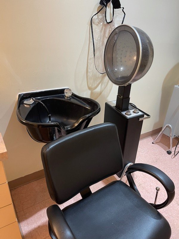 A hair salon station featuring a chair, sink, and overhead hair dryer.