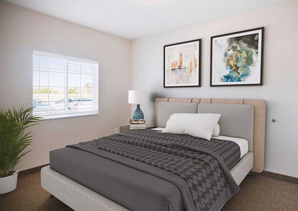 A modern bedroom with a neatly made bed, artwork on the wall, and a bedside lamp.