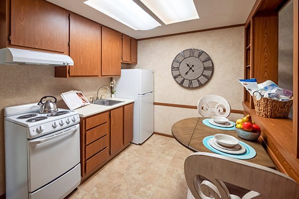A cozy apartment kitchen with wooden cabinets, a dining table set, and a large wall clock.
