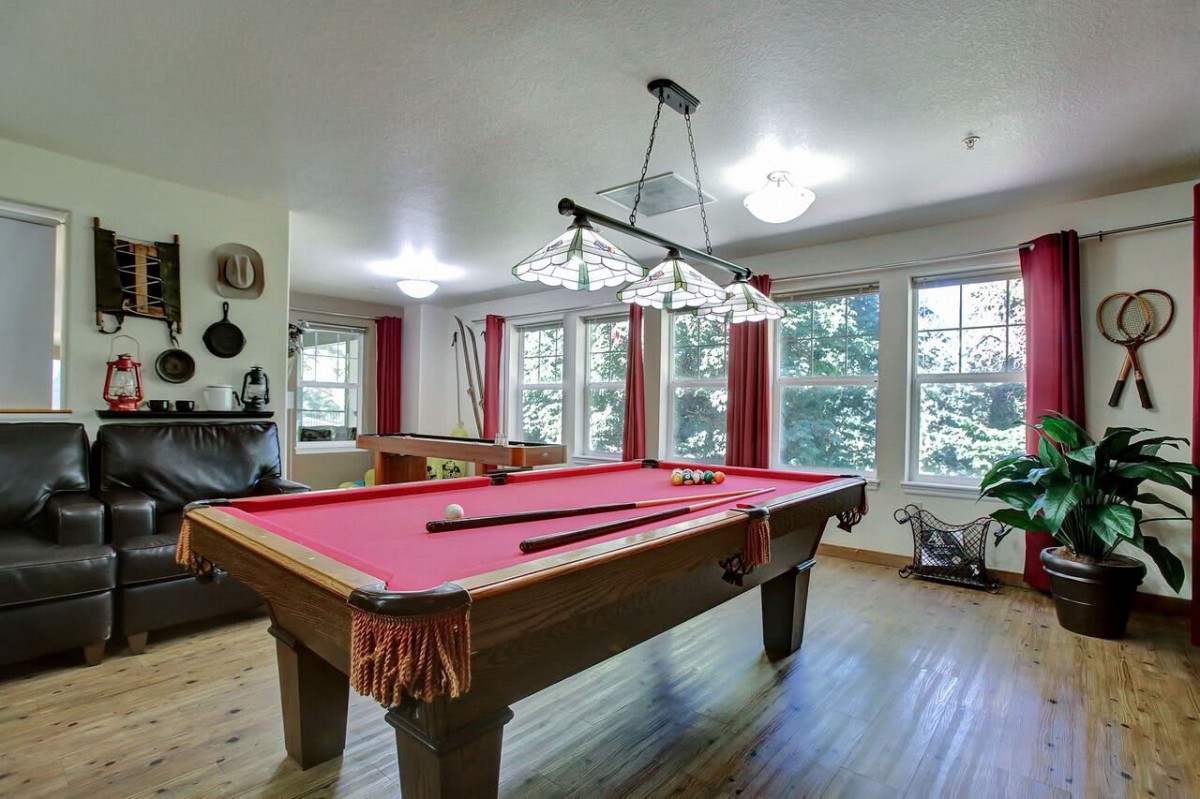 A well-lit billiard room featuring a red pool table and large windows.