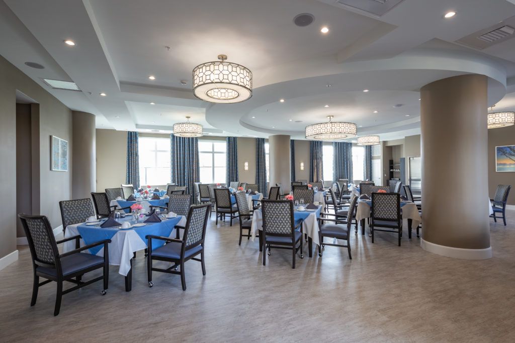 An elegant dining room with well-arranged tables and chairs, adorned with chandeliers and large windows.