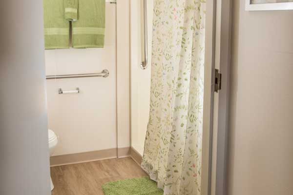 A clean and bright bathroom with green accents, featuring a shower curtain, towels, handrail, and bath mat.