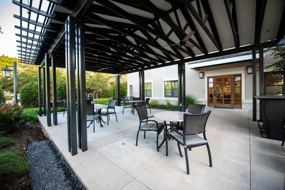 A modern outdoor seating area under a pergola with several tables and chairs.