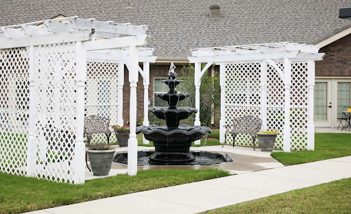 A serene garden scene featuring a black fountain surrounded by white trellises and seating areas.