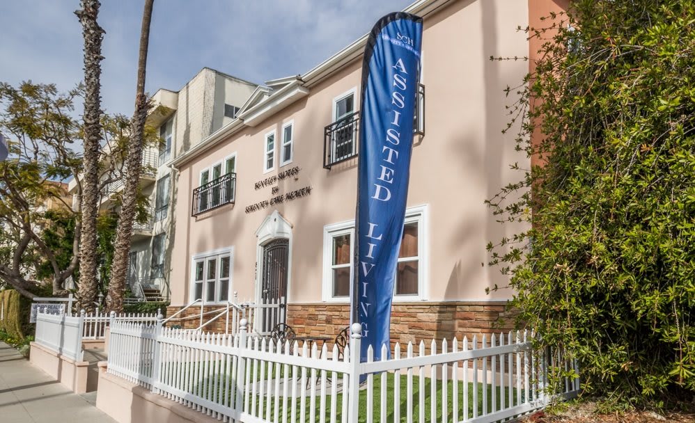 An assisted living facility with a welcoming front yard and a blue flag indicating its purpose.