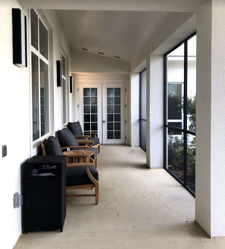 A covered porch with chairs and large windows, leading to double doors.