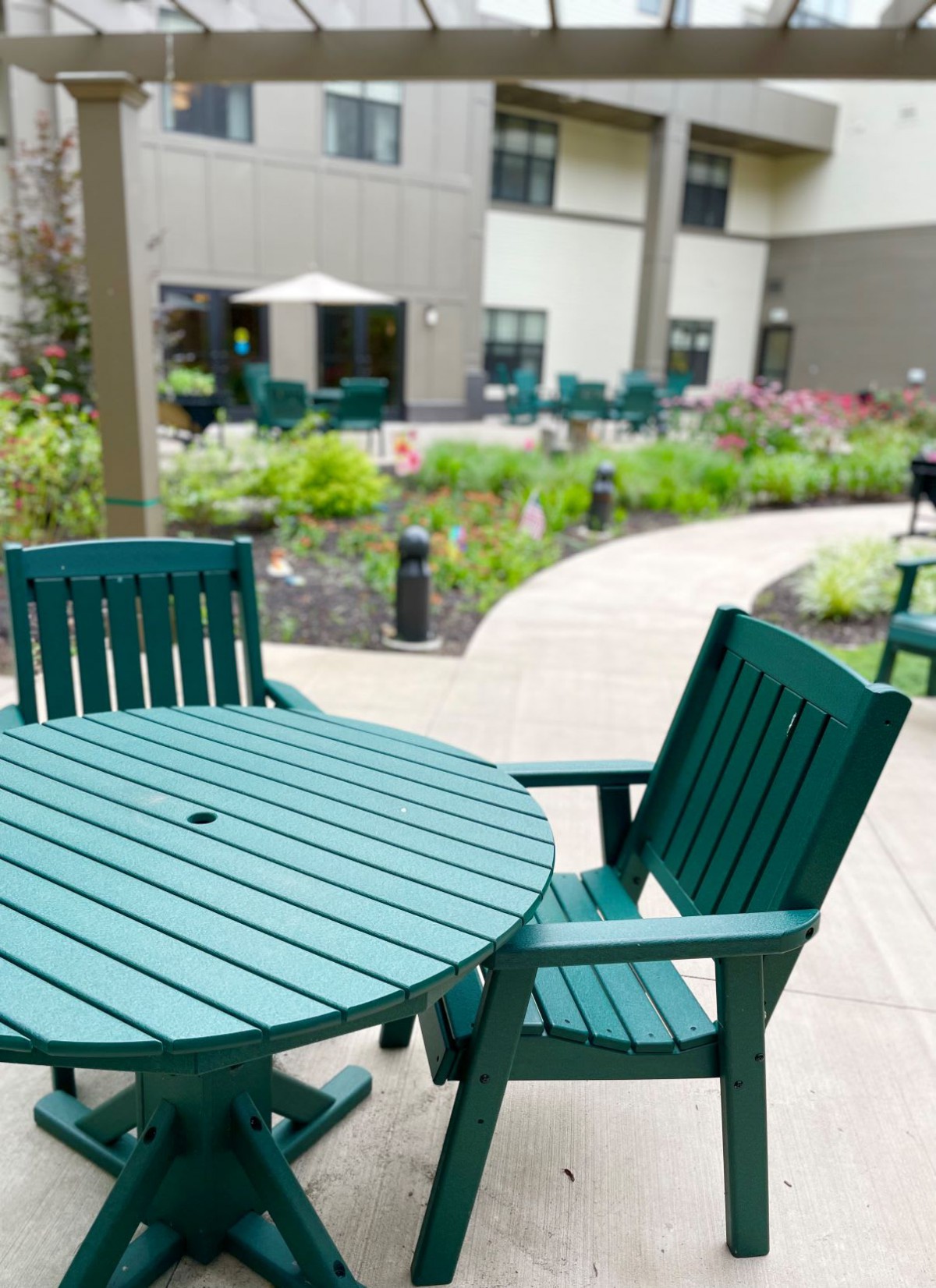 An outdoor patio area featuring green tables and chairs with a garden pathway.