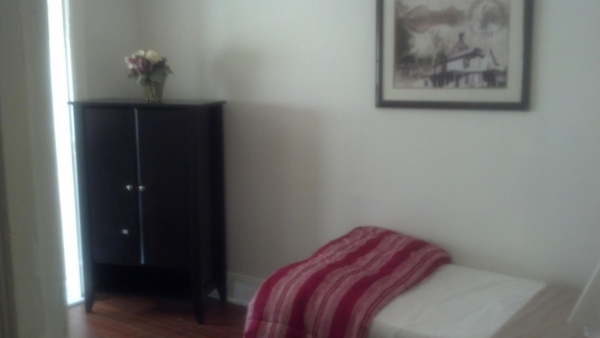 A minimalist bedroom with a single bed, cabinet, and wall art.