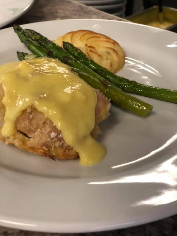 A plated dish featuring meat topped with sauce, alongside asparagus and a potato.