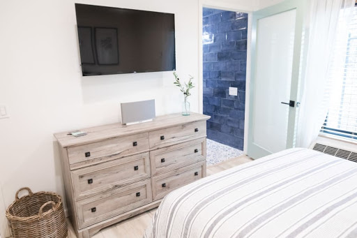 A contemporary bedroom featuring a flat-screen TV mounted on the wall, a stylish dresser, and access to a bathroom.