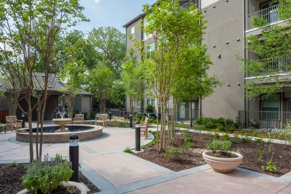 A modern courtyard featuring landscaped gardens, benches, and a central fountain.