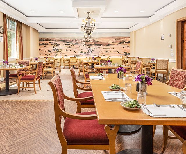 A well-decorated dining area with neatly arranged tables and chairs, featuring elegant lighting and wall art.