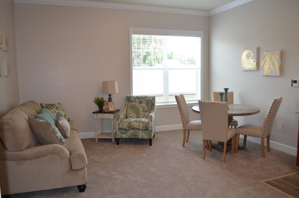 A cozy living room with a dining area, featuring comfortable seating and a large window.