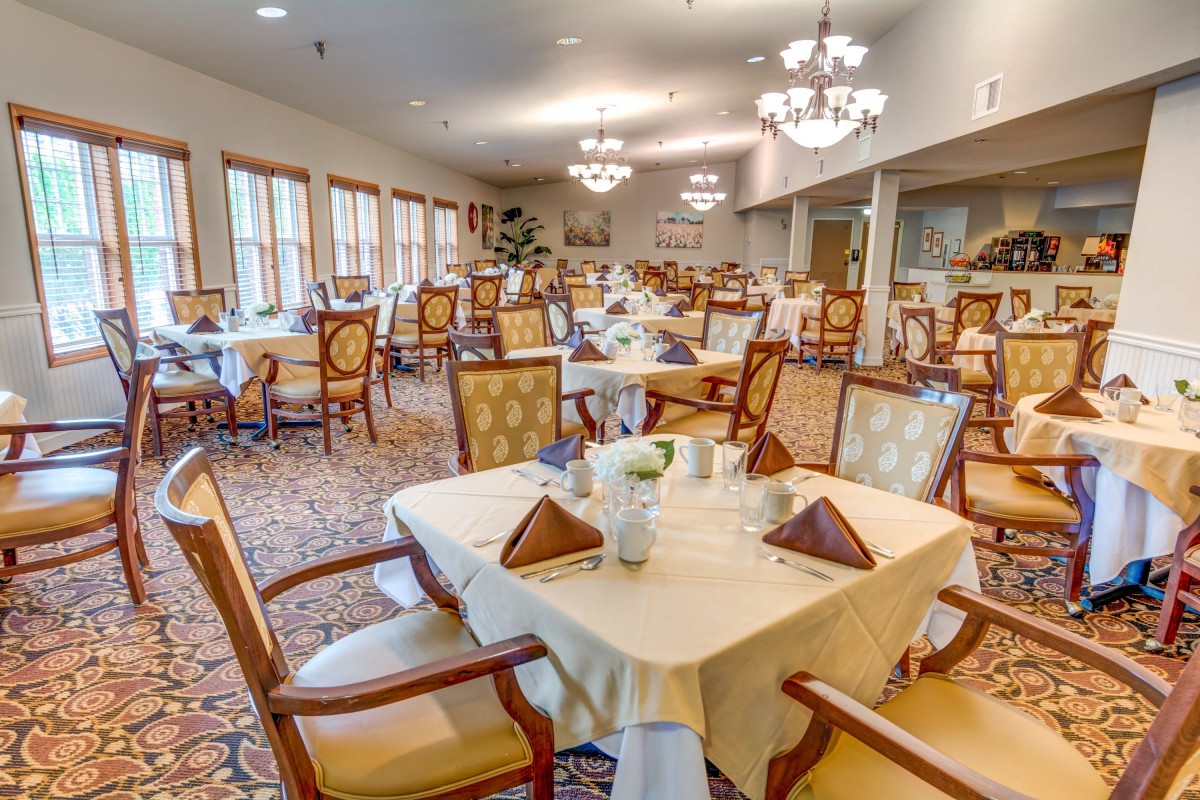An elegant dining room with neatly arranged tables and chairs, illuminated by chandeliers.