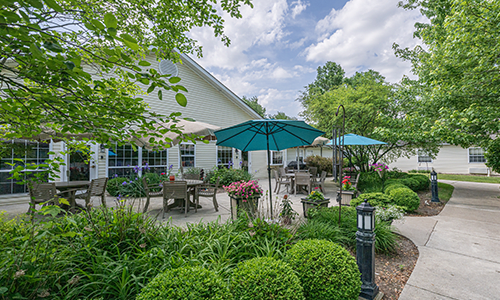 A beautiful outdoor patio area with tables, chairs, and umbrellas surrounded by lush greenery.