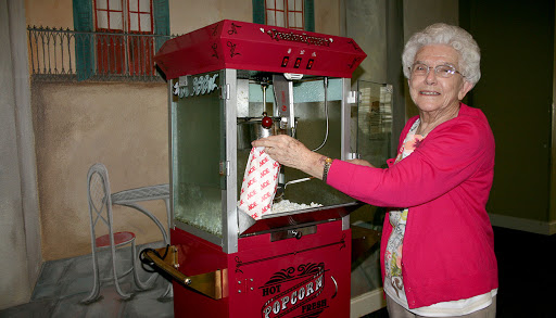An elderly woman serves popcorn from a vintage popcorn machine.