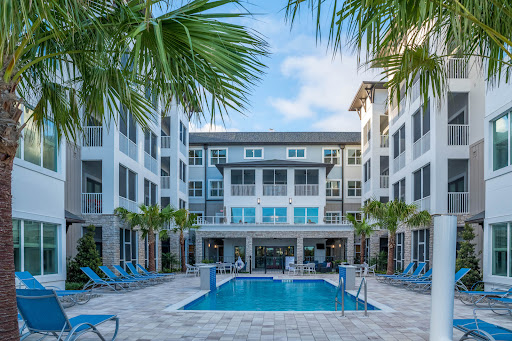 A serene view of a modern apartment complex featuring a swimming pool surrounded by palm trees.