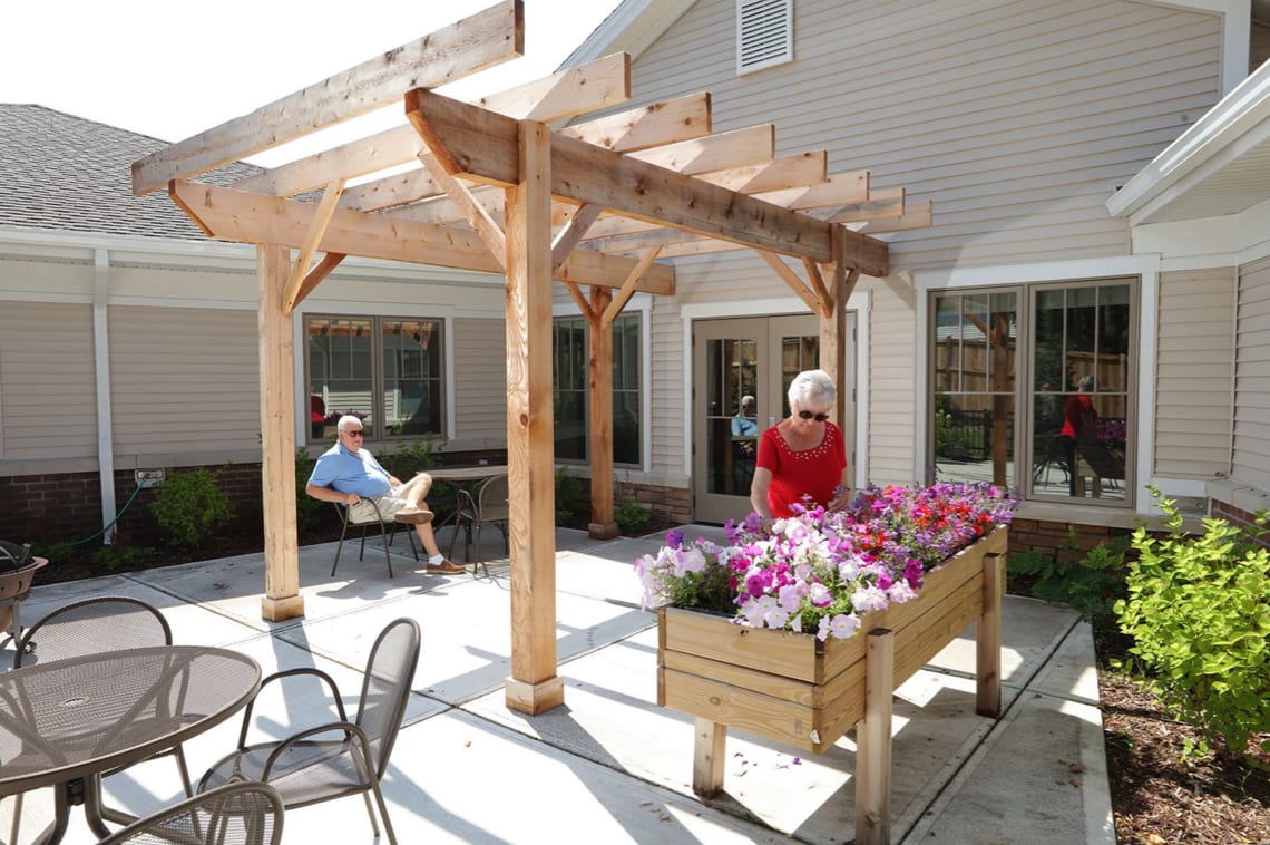 A pergola-covered patio with seating and a flower planter.