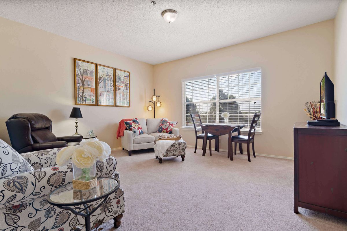 A cozy living room with a sofa, chairs, and a table by the window adorned with decorative artwork.