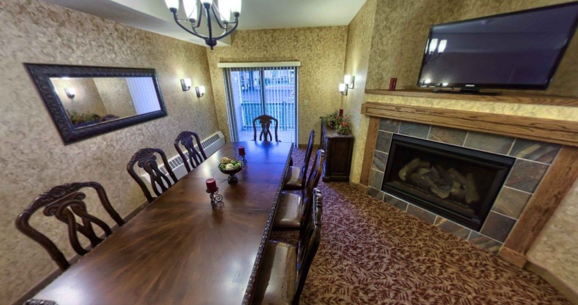A cozy dining room featuring a long wooden table, elegant chairs, and a warm fireplace.