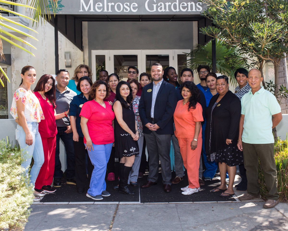 A group of staff members stands together in front of Melrose Gardens.