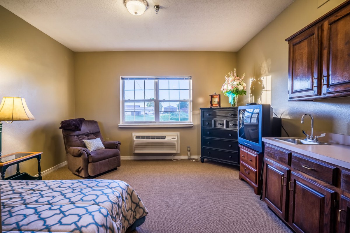 A cozy bedroom with an armchair, dresser, and television next to a window.