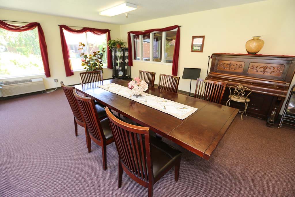 A well-furnished dining room with a large wooden table and chairs, adorned with decorative elements and natural light from large windows.