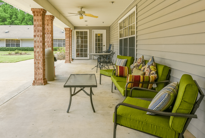 A cozy patio with green cushioned seating and a glass-topped table under a covered porch.